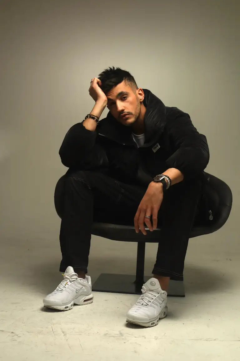 Portrait de Kader Bueno, magicien et humoriste, assis sur un fauteuil noir