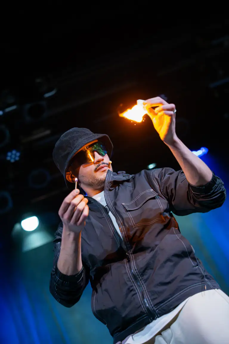 Kader Bueno, magicien, sur scène avec une allumette et un papier qui brûle