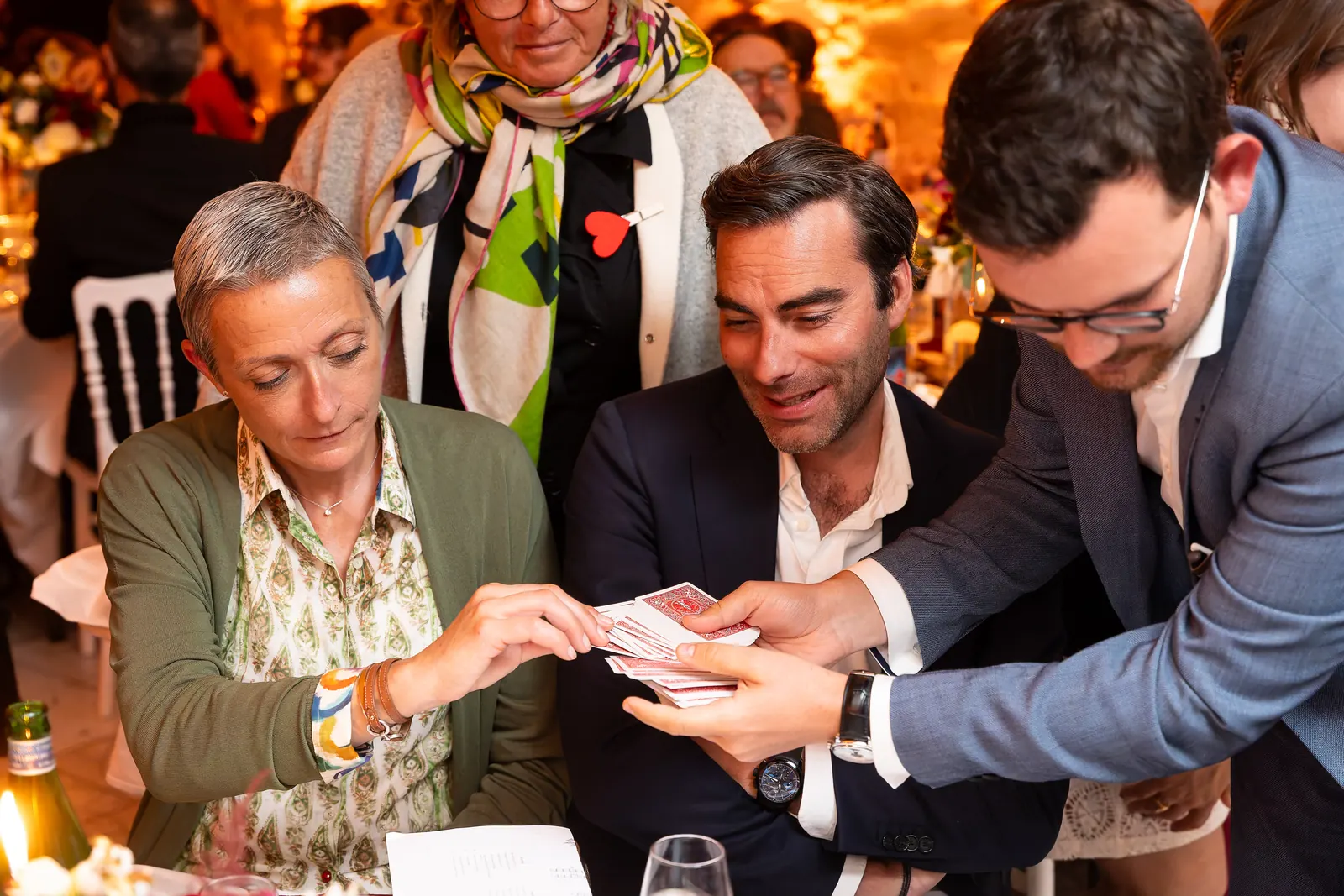 Alexis fait un tour de cartes à une invitée et deux convives pendant un dîner