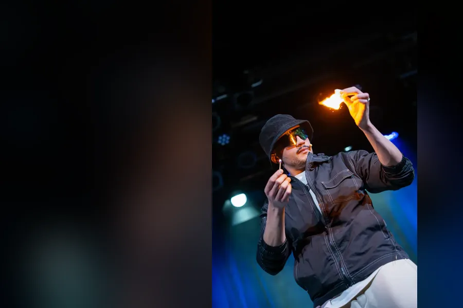 Kader Bueno sur scène, une allumette et un papier enflammés entre les mains