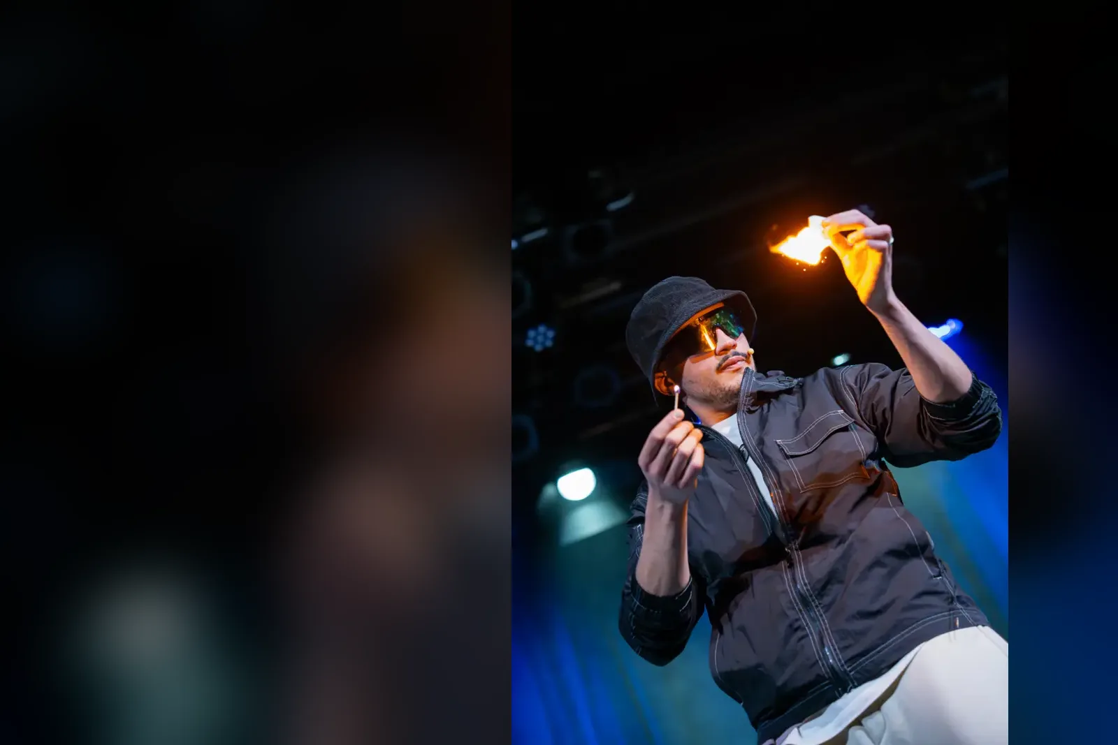 Kader Bueno sur scène, une allumette et un papier enflammés entre les mains