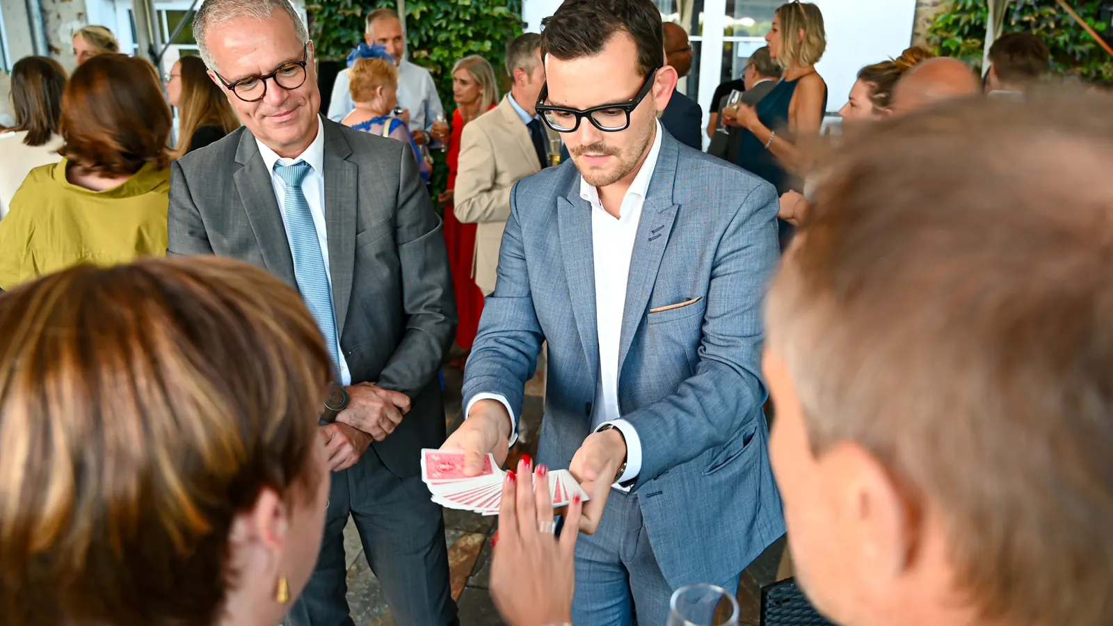 Alexis présente un éventail de cartes à des invités pendant un cocktail